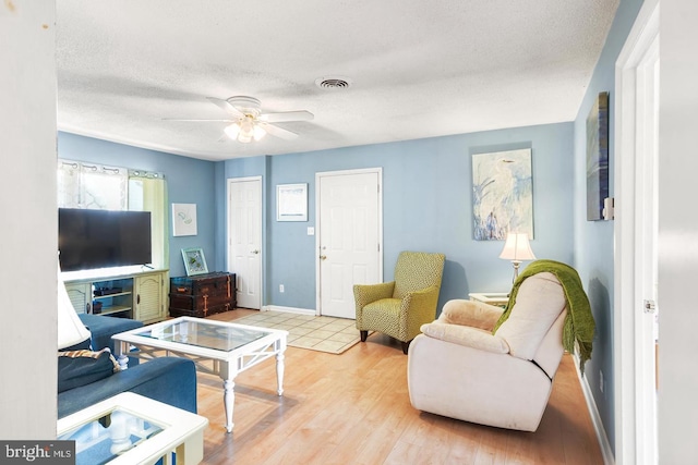 living room with light wood-type flooring, ceiling fan, and a textured ceiling