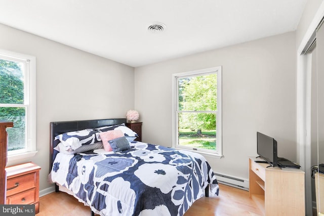 bedroom with baseboard heating, light hardwood / wood-style flooring, and a closet