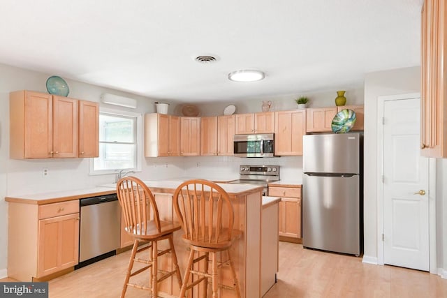 kitchen with appliances with stainless steel finishes, a center island, light brown cabinetry, a kitchen breakfast bar, and light wood-type flooring