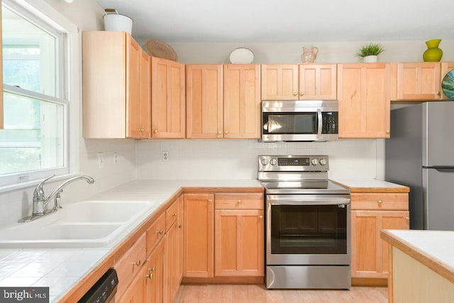 kitchen with light brown cabinetry, sink, light wood-type flooring, backsplash, and stainless steel appliances