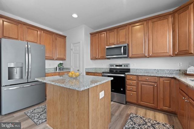 kitchen featuring stainless steel appliances, a center island, light wood-type flooring, and light stone countertops