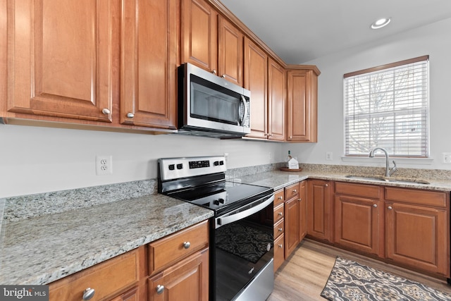 kitchen with sink, light hardwood / wood-style flooring, light stone counters, and appliances with stainless steel finishes