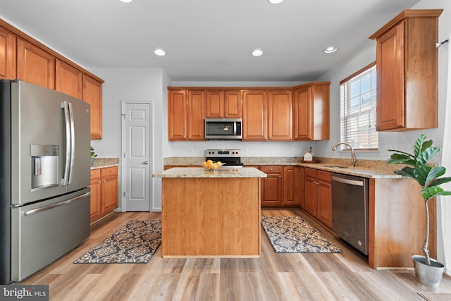 kitchen featuring appliances with stainless steel finishes, a center island, light stone countertops, sink, and light hardwood / wood-style flooring