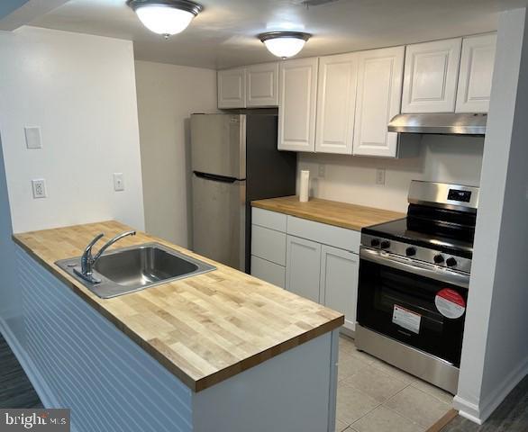 kitchen featuring wooden counters, white cabinets, stainless steel appliances, kitchen peninsula, and sink