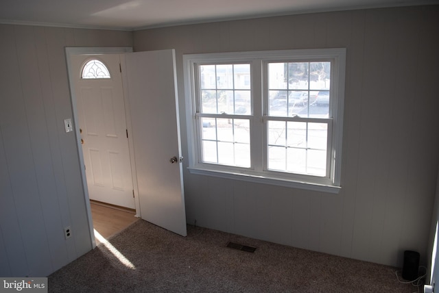 carpeted foyer with a wealth of natural light, ornamental molding, and wood walls