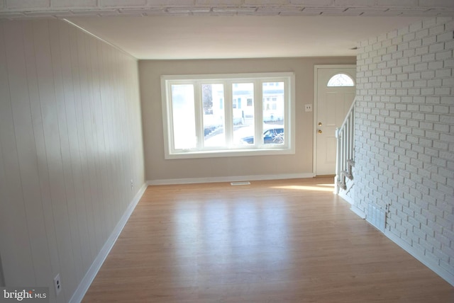 unfurnished living room featuring plenty of natural light, wood walls, brick wall, and light hardwood / wood-style flooring