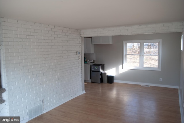 unfurnished living room with hardwood / wood-style flooring and brick wall