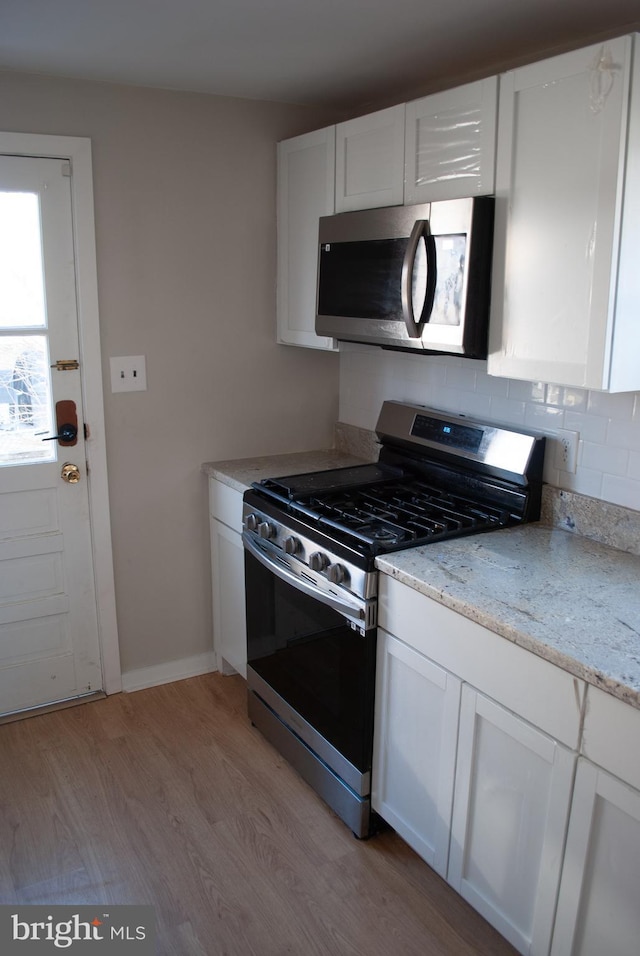 kitchen with light stone counters, white cabinets, light hardwood / wood-style floors, and appliances with stainless steel finishes