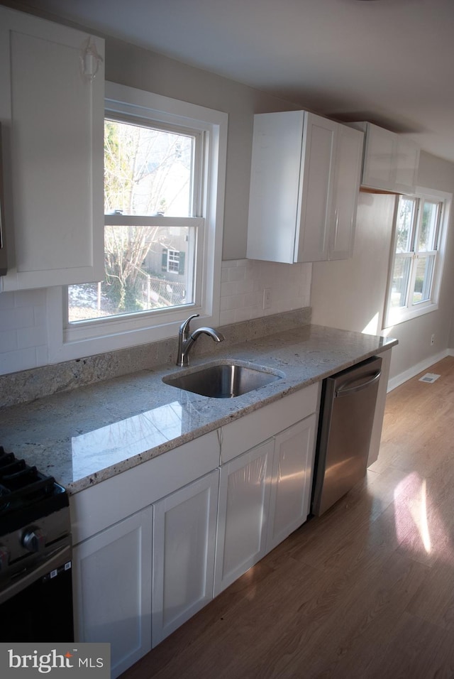 kitchen featuring stainless steel dishwasher, white cabinets, light stone countertops, and sink