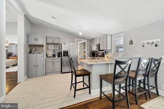 kitchen featuring lofted ceiling, stainless steel appliances, kitchen peninsula, a breakfast bar, and gray cabinetry