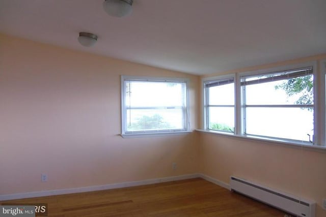 empty room featuring wood-type flooring, a baseboard radiator, and vaulted ceiling