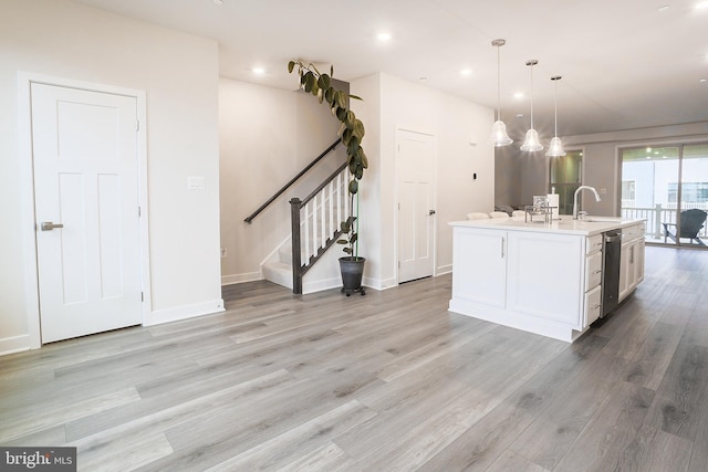 kitchen featuring decorative light fixtures, dishwasher, white cabinets, a kitchen island with sink, and light hardwood / wood-style flooring