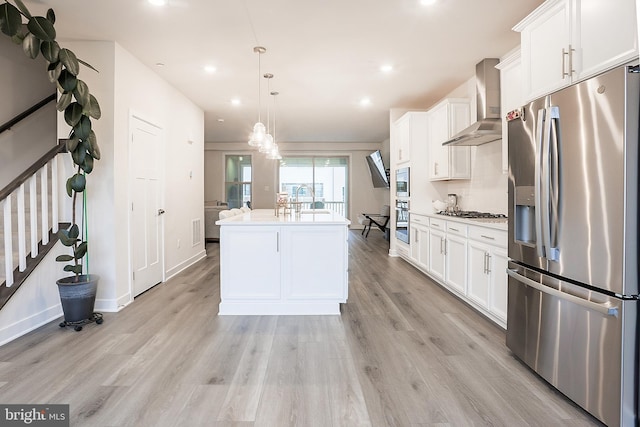 kitchen with appliances with stainless steel finishes, pendant lighting, wall chimney range hood, a kitchen island with sink, and white cabinets