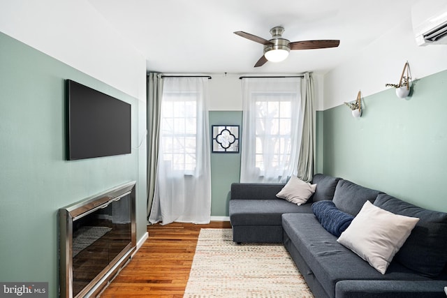 living room featuring a wall unit AC, ceiling fan, and wood-type flooring