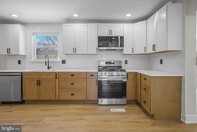 kitchen featuring appliances with stainless steel finishes, decorative backsplash, white cabinets, light hardwood / wood-style flooring, and sink