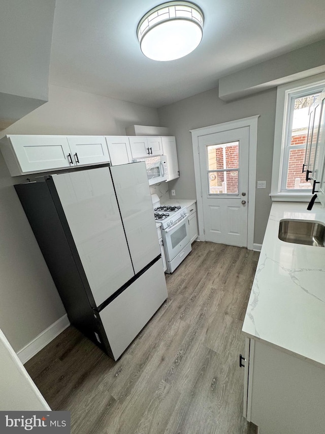 kitchen with light stone counters, sink, white cabinets, and white appliances