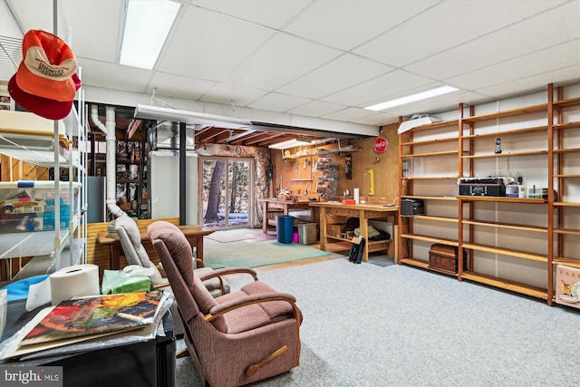 basement featuring a workshop area, wooden walls, a drop ceiling, and carpet