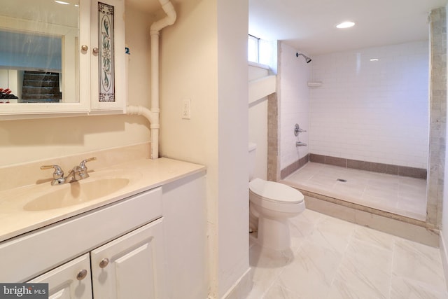 bathroom featuring a tile shower, vanity, and toilet