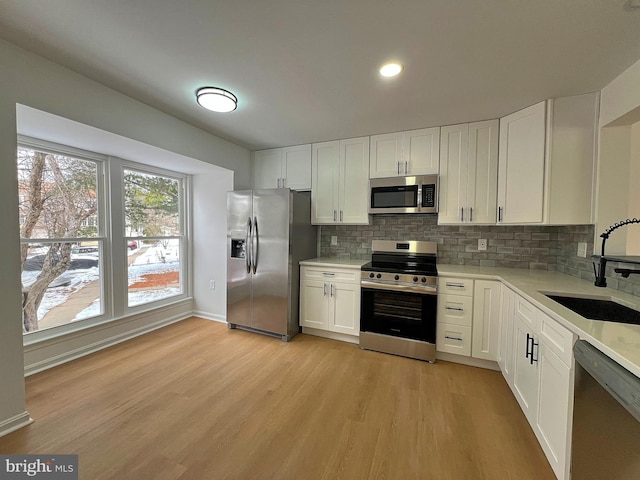 kitchen featuring backsplash, stainless steel appliances, sink, light hardwood / wood-style floors, and white cabinetry