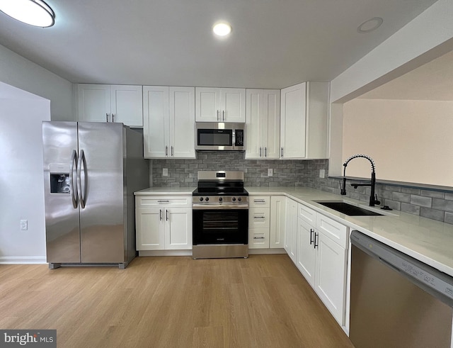 kitchen featuring decorative backsplash, stainless steel appliances, sink, light hardwood / wood-style flooring, and white cabinets