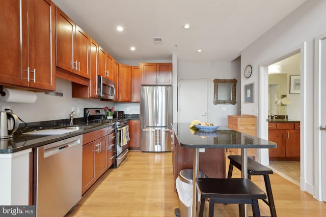 kitchen featuring a breakfast bar area, light wood-type flooring, stainless steel appliances, a center island, and sink