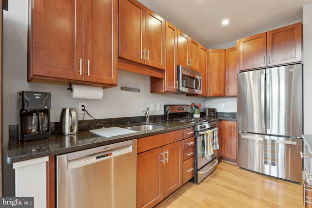 kitchen with sink, appliances with stainless steel finishes, dark stone counters, and light wood-type flooring