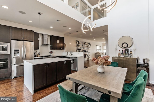 kitchen with a center island, stainless steel appliances, wall chimney range hood, dark hardwood / wood-style flooring, and decorative light fixtures