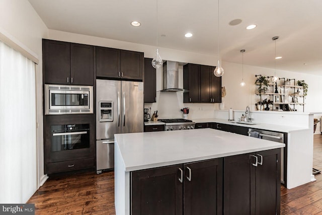 kitchen with wall chimney exhaust hood, stainless steel appliances, sink, a center island, and hanging light fixtures