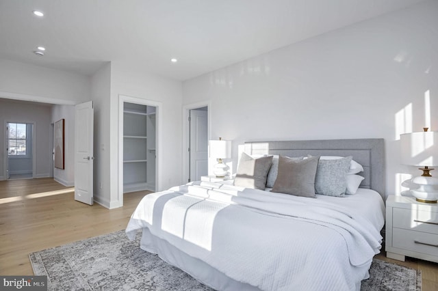 bedroom with a walk in closet, light hardwood / wood-style flooring, and a closet