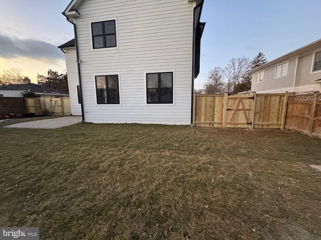 back house at dusk with a lawn and a patio