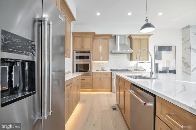 kitchen with pendant lighting, sink, wall chimney range hood, tasteful backsplash, and premium appliances