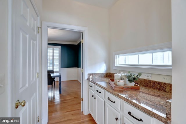 kitchen featuring white cabinets, light hardwood / wood-style flooring, stone countertops, and ornamental molding