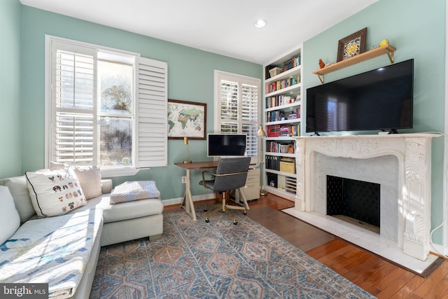 living room with hardwood / wood-style flooring, built in shelves, and a premium fireplace