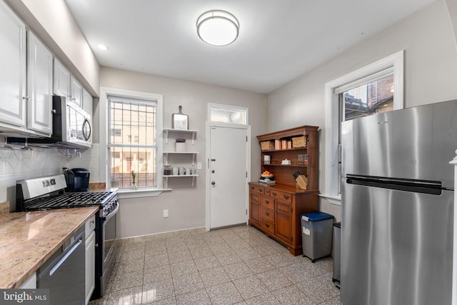 kitchen featuring light stone counters, appliances with stainless steel finishes, white cabinetry, and tasteful backsplash