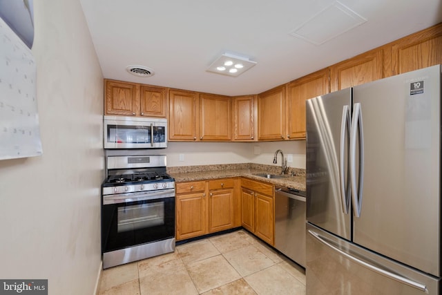 kitchen with light tile patterned flooring, stainless steel appliances, light stone counters, and sink