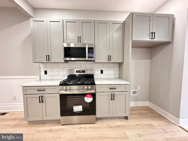 kitchen with backsplash, gray cabinets, light stone counters, and stainless steel appliances