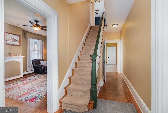 stairway featuring a baseboard heating unit, ceiling fan, and hardwood / wood-style floors