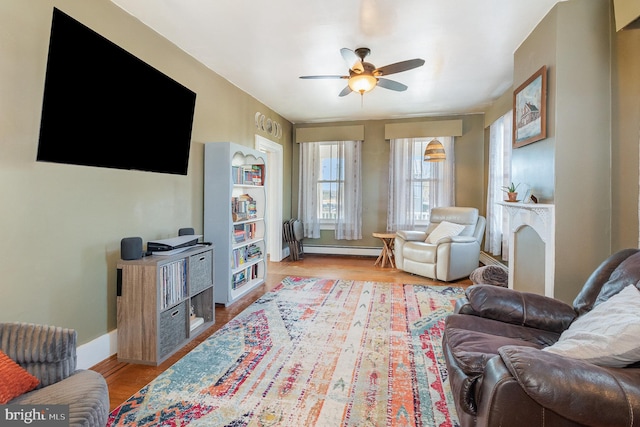 living room featuring baseboard heating, a fireplace, light hardwood / wood-style flooring, and ceiling fan