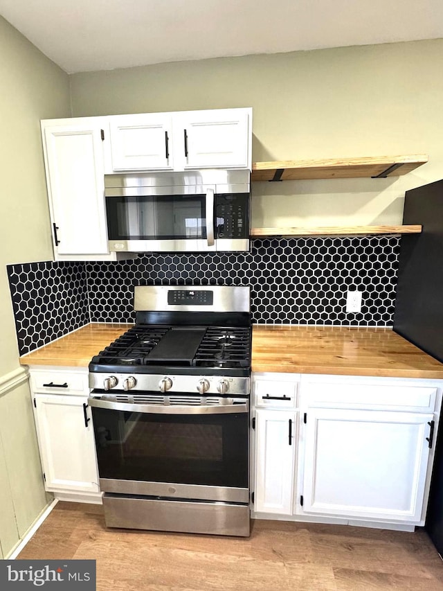 kitchen with white cabinets, light wood-type flooring, stainless steel appliances, and tasteful backsplash