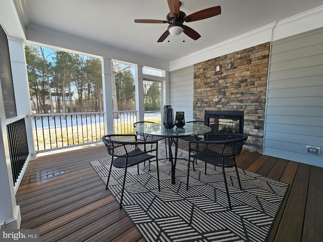 sunroom with ceiling fan, an outdoor stone fireplace, and a water view