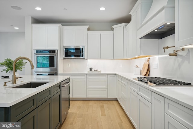 kitchen featuring white cabinetry, stainless steel appliances, sink, light wood-type flooring, and custom range hood