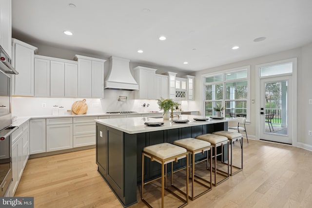 kitchen with white cabinets, a kitchen breakfast bar, premium range hood, and a kitchen island