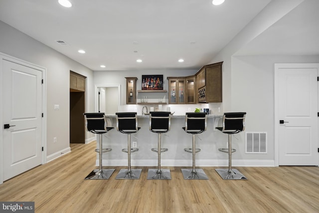 kitchen with a kitchen bar, sink, kitchen peninsula, light hardwood / wood-style flooring, and dark brown cabinets