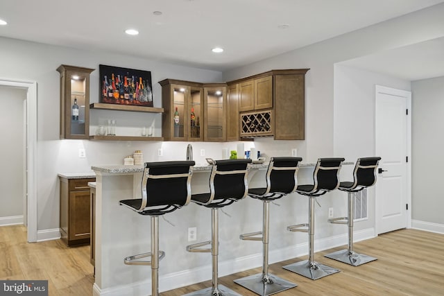 bar with light hardwood / wood-style floors and light stone counters