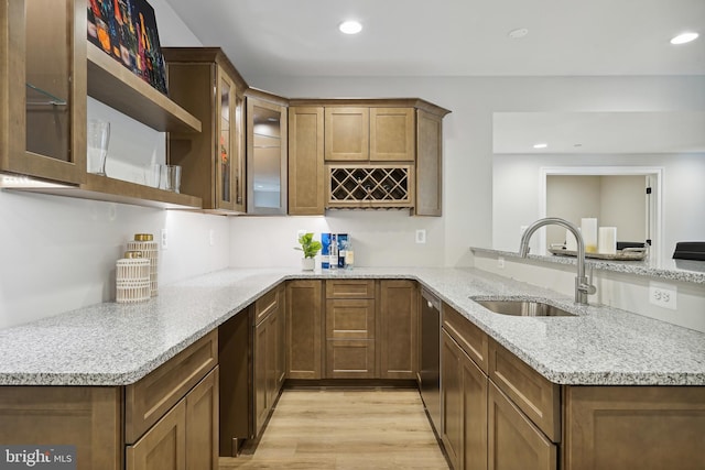 kitchen with light wood-type flooring, kitchen peninsula, sink, and light stone counters