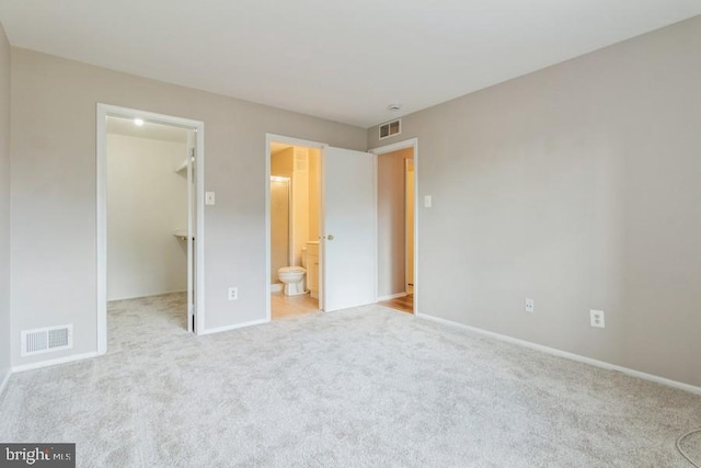 unfurnished bedroom with light colored carpet, a spacious closet, a closet, and ensuite bath