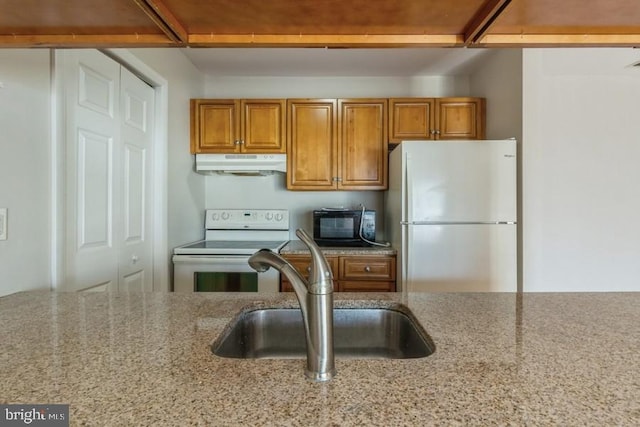 kitchen with white appliances, light stone counters, and sink