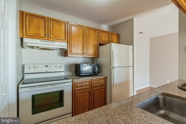 kitchen with white appliances, light stone countertops, and sink