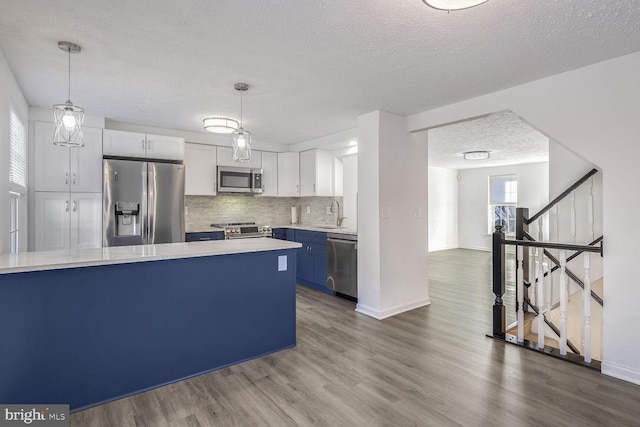 kitchen featuring decorative light fixtures, stainless steel appliances, blue cabinets, and white cabinetry