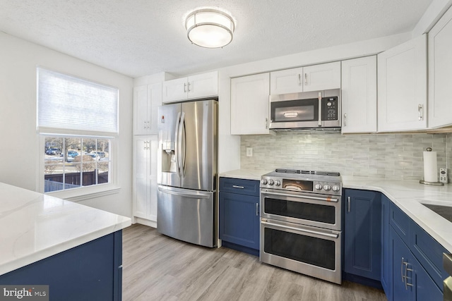 kitchen with stainless steel appliances, tasteful backsplash, light wood-type flooring, blue cabinets, and white cabinets